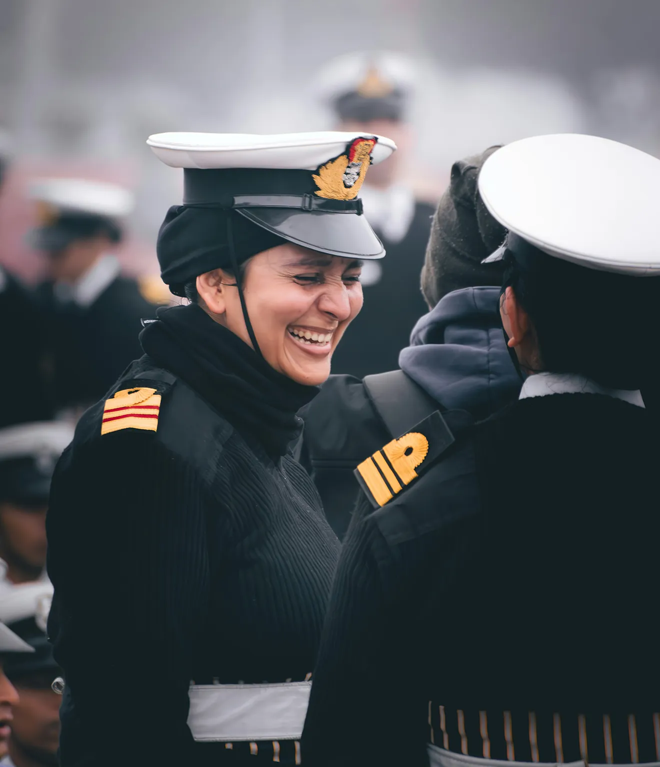 Smiling female naval officer in uniform and white cap talking to another officer.